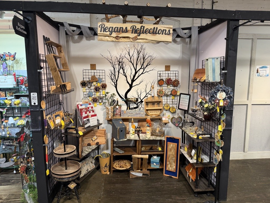 Regans Reflections vendor space at Market Street Creatives with hanging sign, gridwall displays and wood shelving